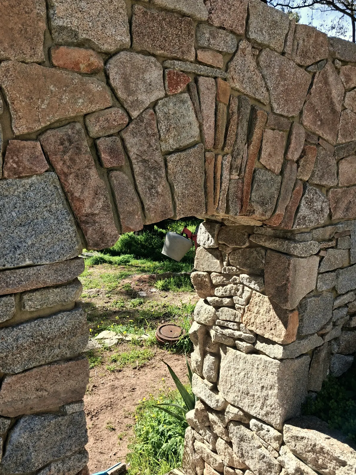 A granite arch built without mortar, opening onto the garden beyond